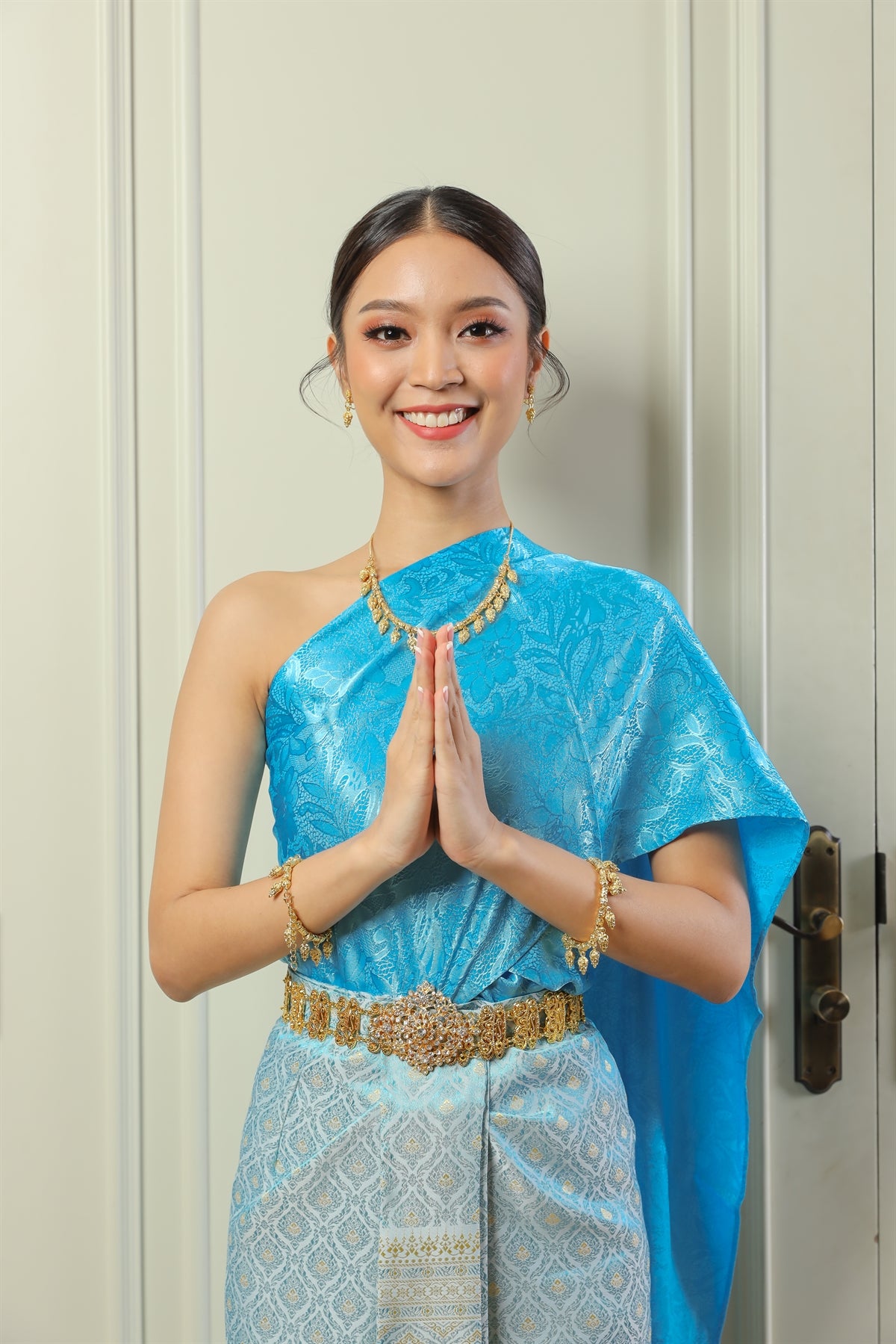 A Thai woman happily greets guests in her traditional Thai dress.